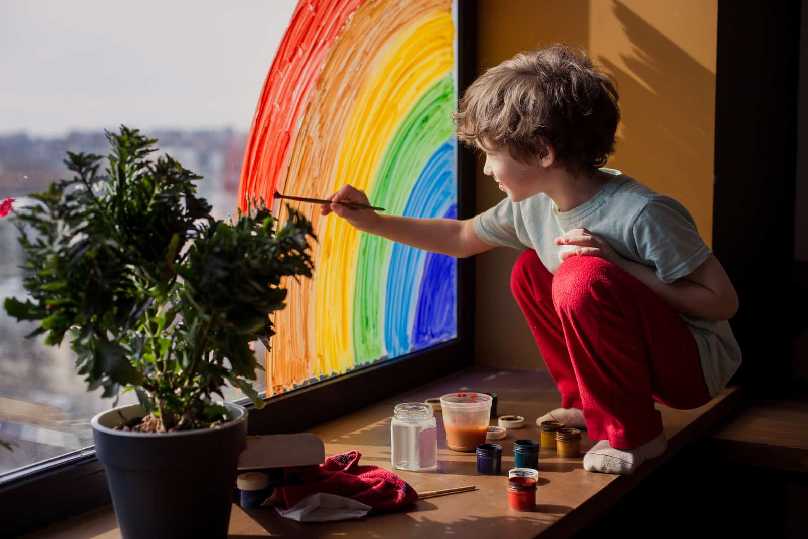 boy painting a rainbow on the window