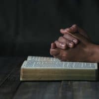 folded hands on top of bible in dark room