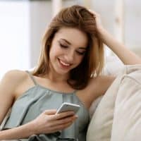 a smiling woman sitting on the couch holding a cell phone in her hand