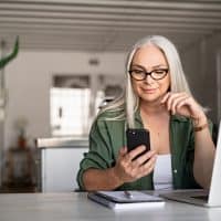 una mujer rubia con gafas en la cabeza sostiene un teléfono móvil en la mano mientras está sentada en una mesa