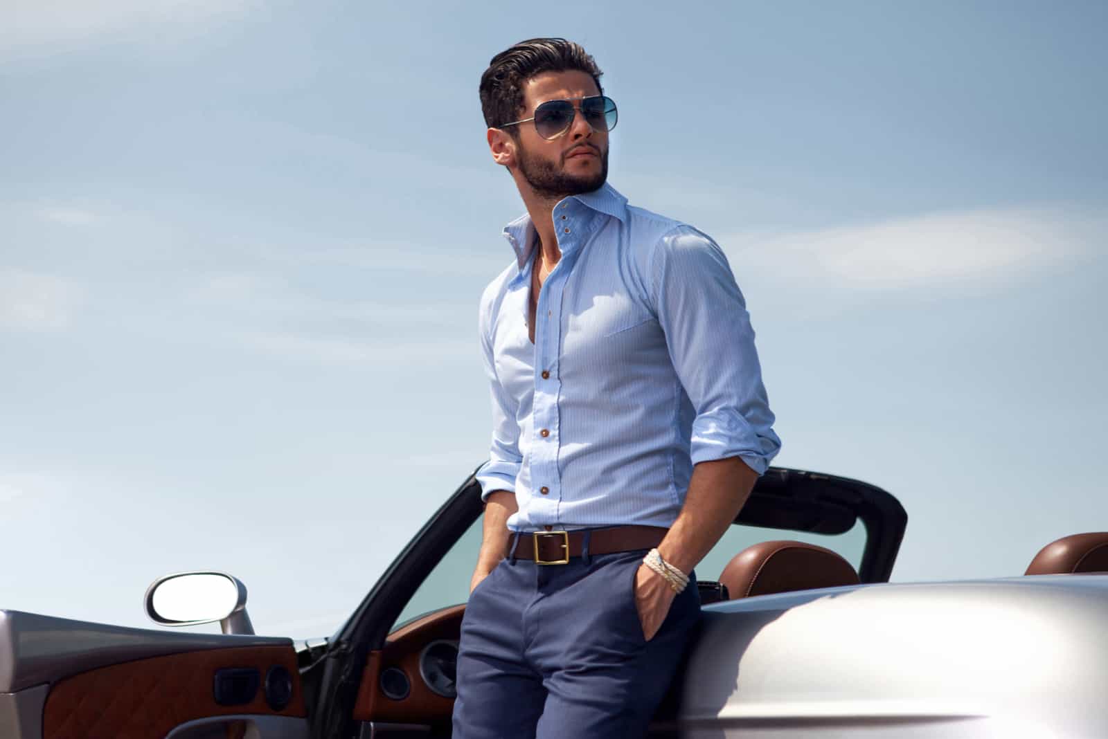 a handsome man leaning against a car and looking away