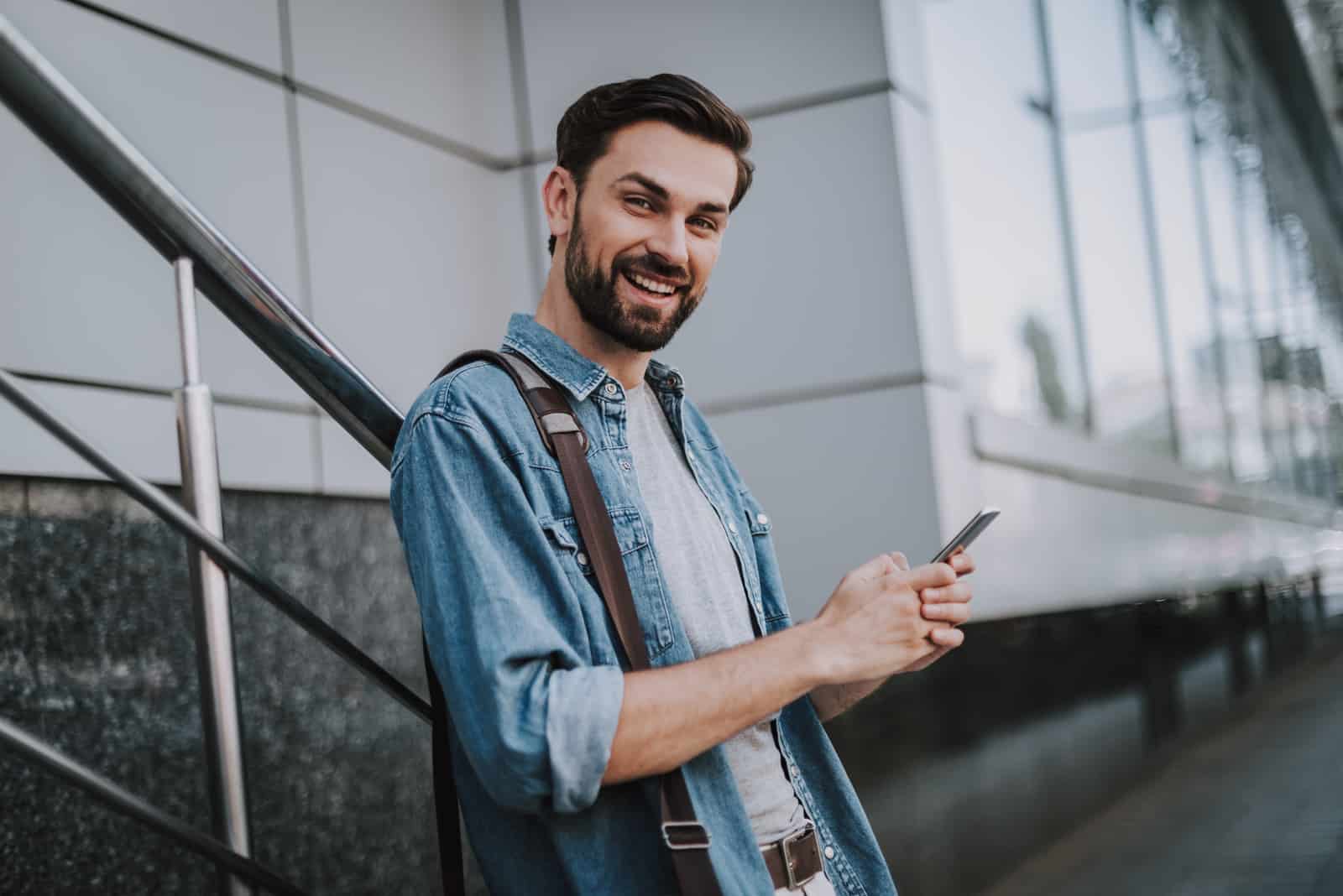 a smiling man leaning against a fence and holding a cell phone in his hand