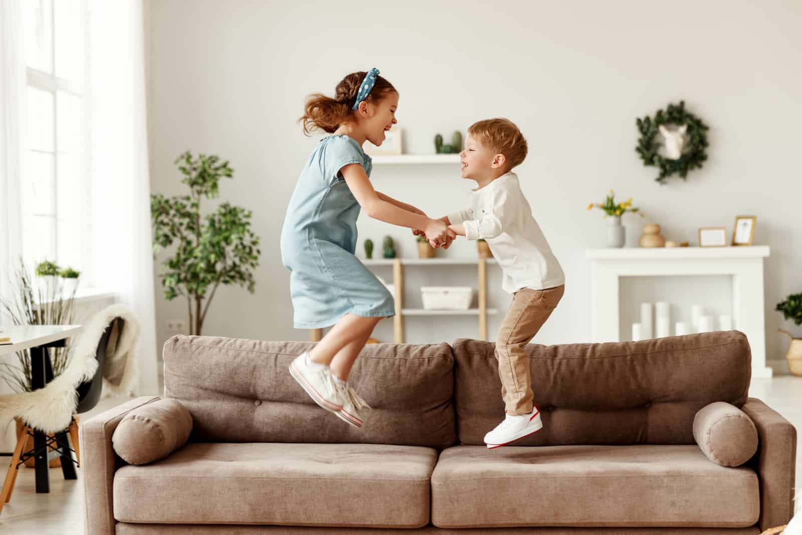 chico y chica alegres cogidos de la mano y saltando en el sofá