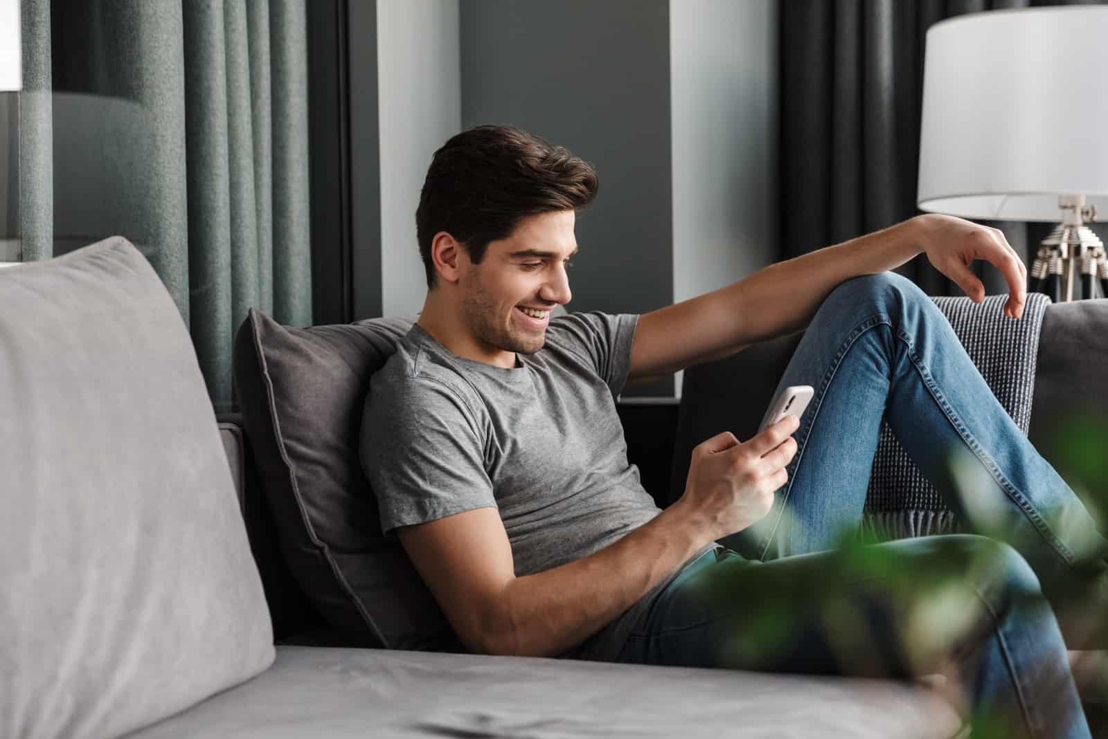 hombre feliz sentado en el sofá y enviando mensajes de texto