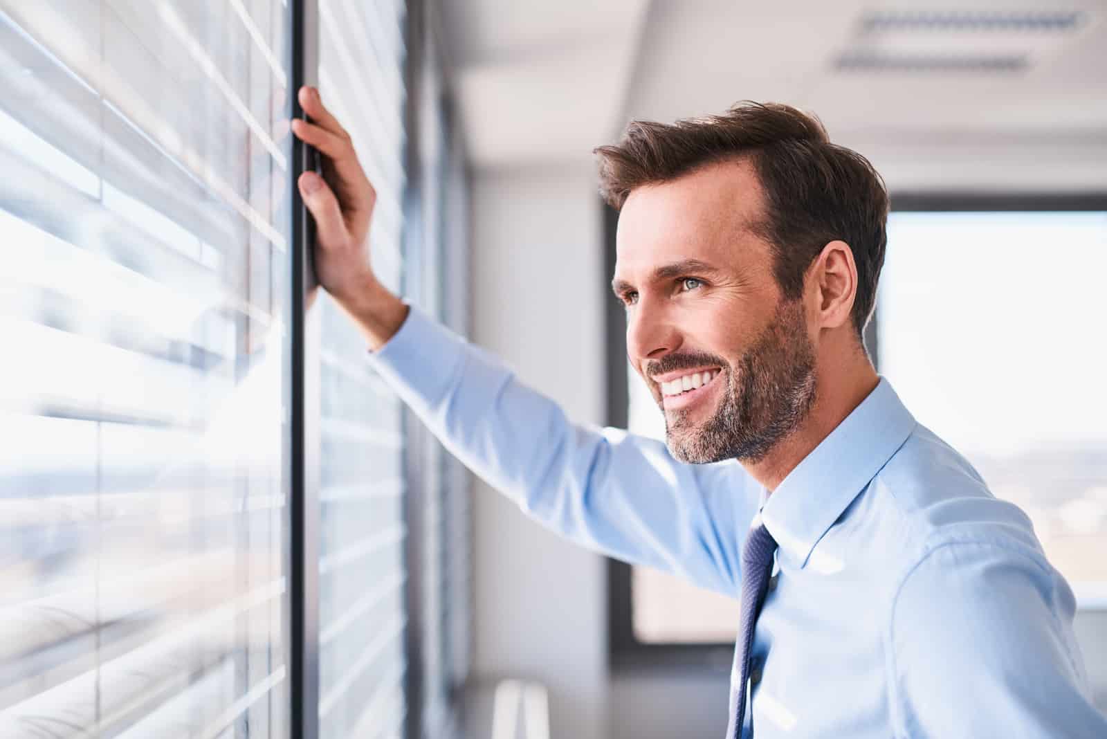 hombre sonriente mirando por la ventana de la oficina