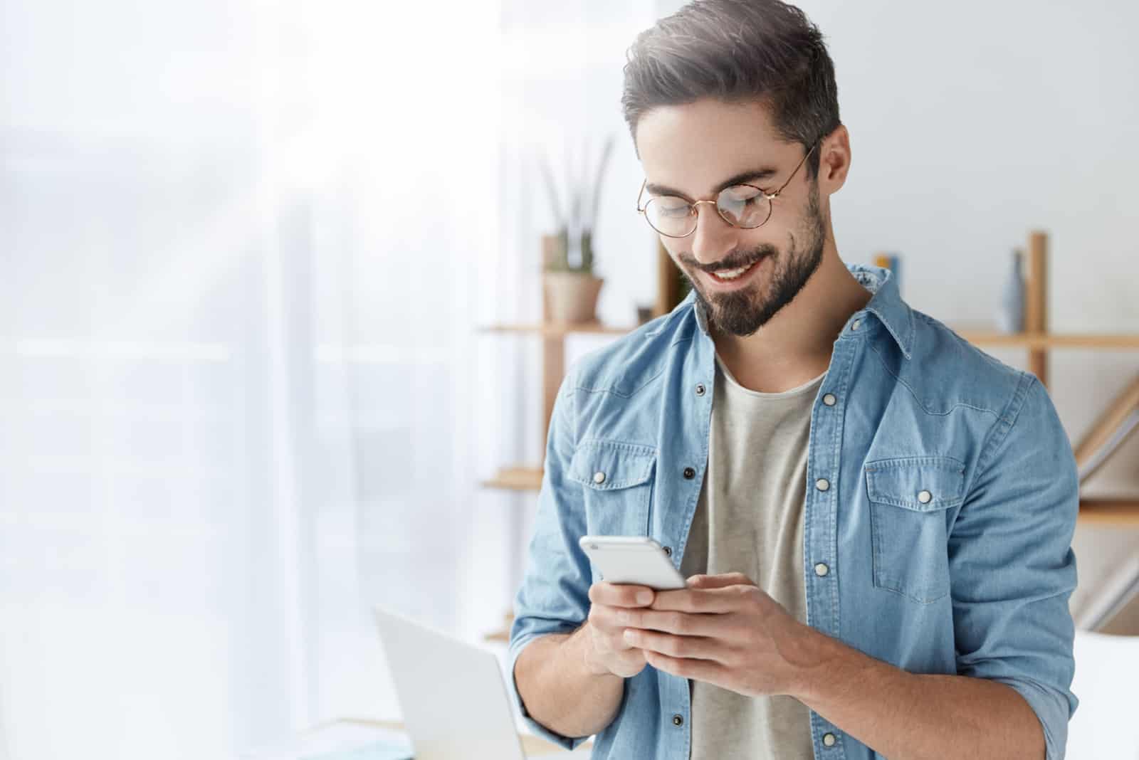 hombre sonriente con gafas escribiendo en el móvil