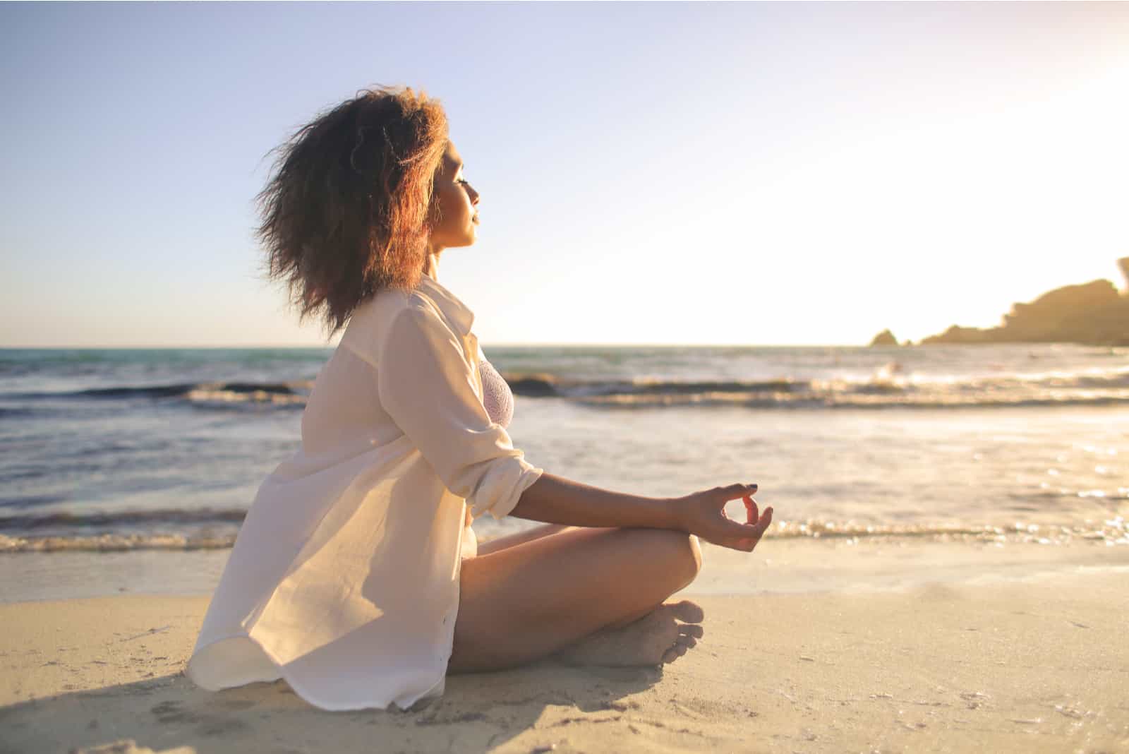 mujer medita en la playa a la luz del sol