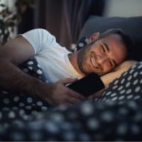 happy man lying in bed texting