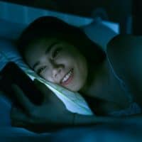 happy woman looking at smartphone in bed at night