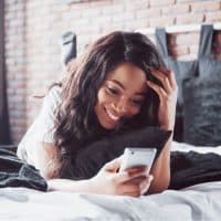 a smiling woman lies on the bed and buttons on the phone