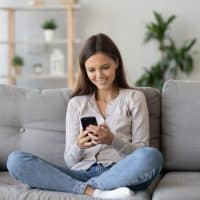 happy girl sitting on sofa texting