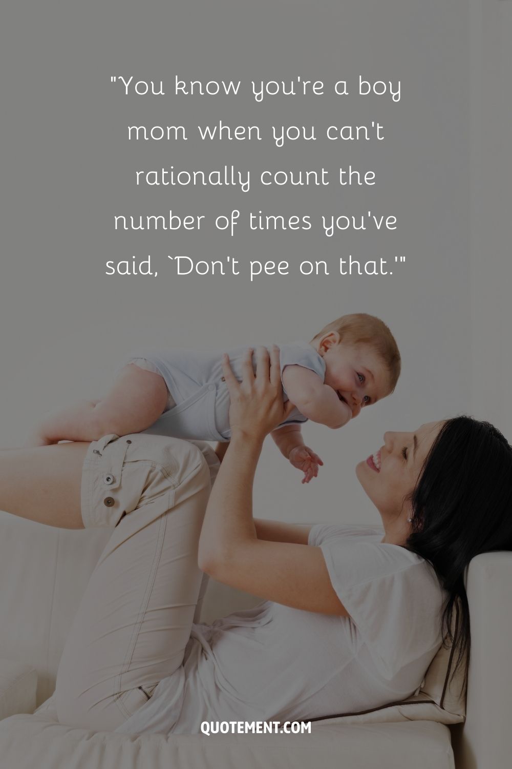 A mother in a relaxed pose on a couch lifts her baby boy into the air