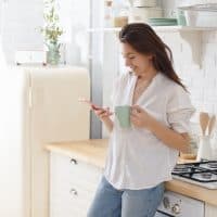 beautiful woman standing in the kitchen and button on the phone
