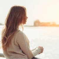 an imaginary girl with long brown hair stands leaning against a bridge and looks into the distance