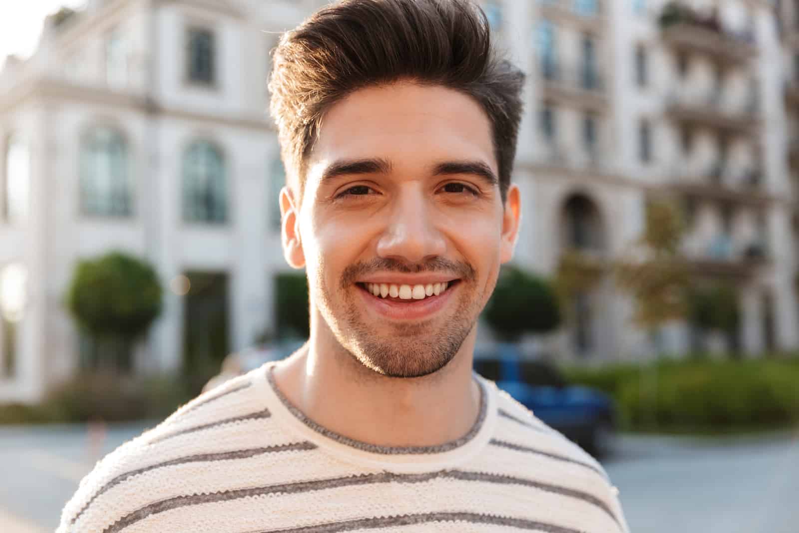 hombre guapo sonriendo y mirando a la cámara mientras camina en la calle de la ciudad