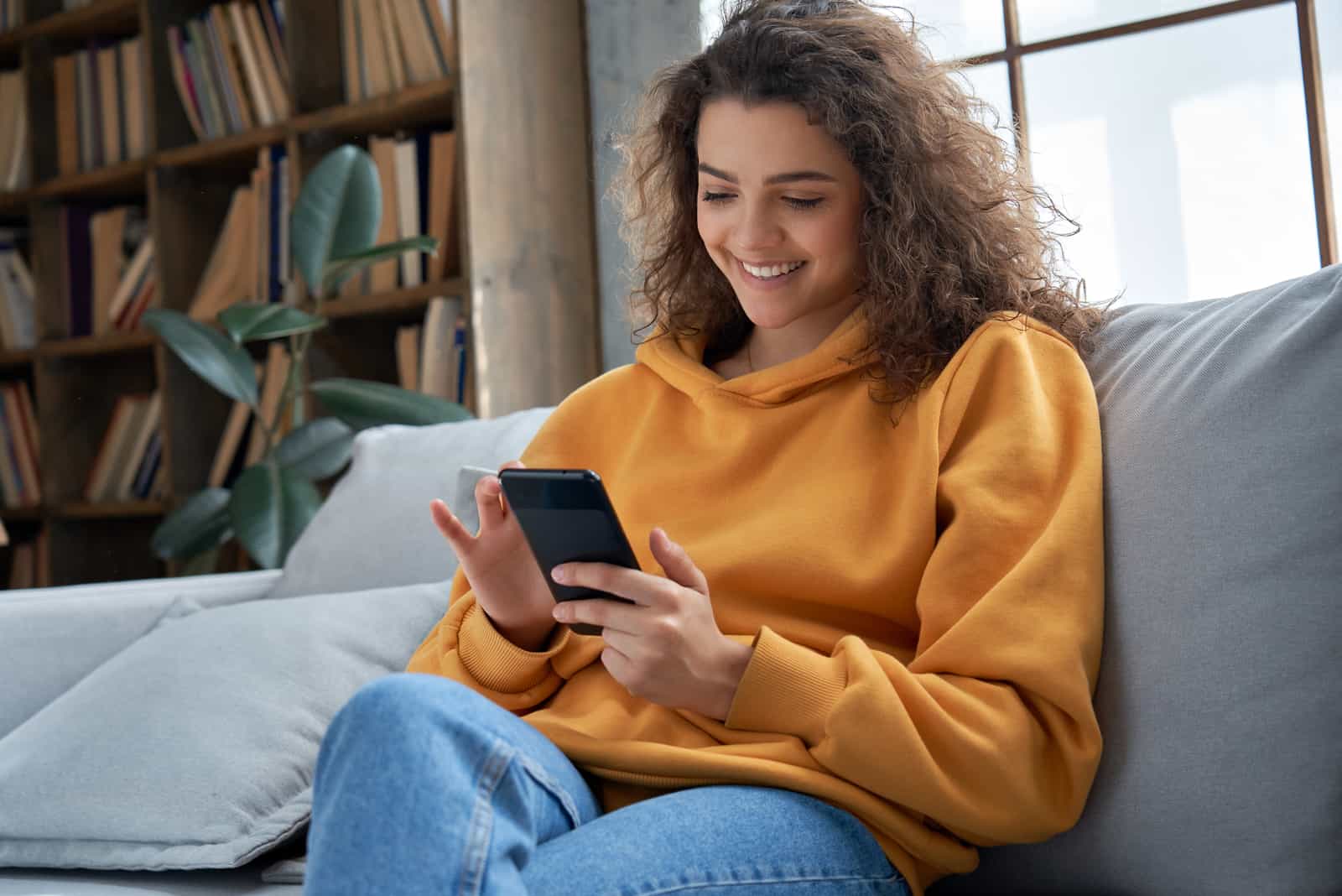 joven feliz enviando mensajes de texto en el sofá de su casa