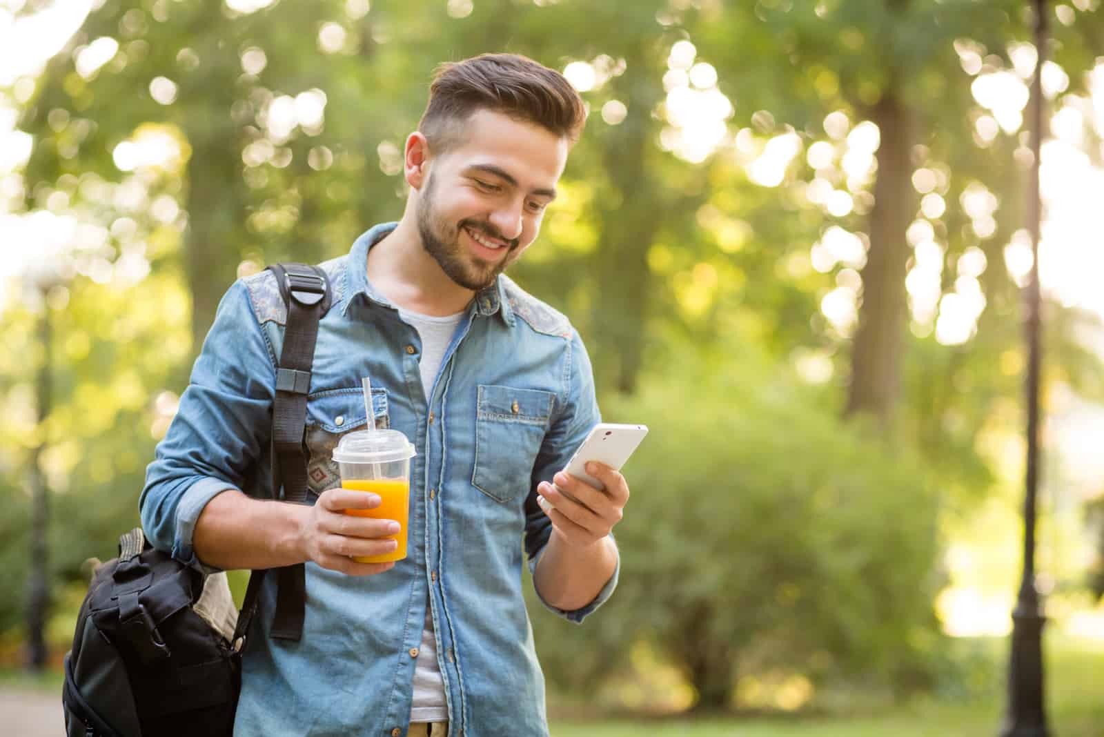 hombre sonriente con zumo en una mano y teléfono móvil en la otra