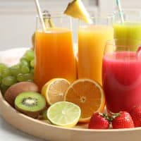 Wooden tray with glasses of different juices and fresh fruits on table