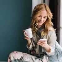 una mujer sonriente sentada junto a la ventana y pulsando el teléfono