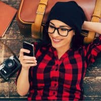 a smiling woman with a hat on her head lies on the pier and a button on the phone