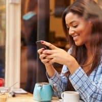 a smiling woman sitting at a table and pressing a phone