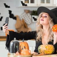 A woman in a witch costume uses a mobile phone to take pictures