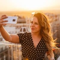 Young blonde woman taking a photo of herself with her phone with sunset