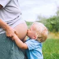 little boy kissing his mom't pregnant belly outdoors