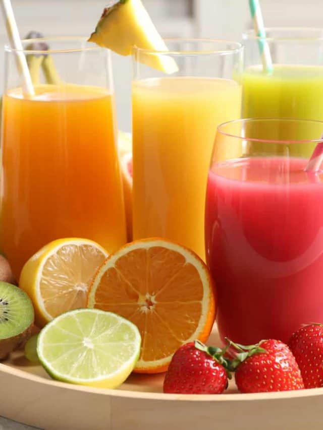 Wooden tray with glasses of different juices and fresh fruits on table