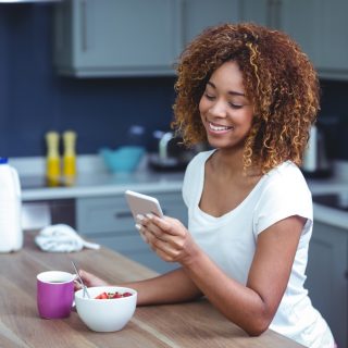 una mujer sonriente está sentada en la cocina y teclea en el teléfono