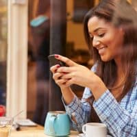 una mujer sonriente está sentada detrás de un trineo y teclea en un teléfono móvil