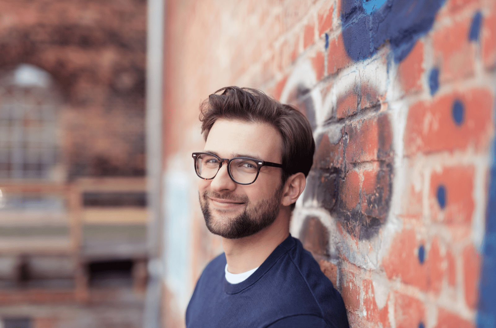 a smiling man leaning against the wall of the house