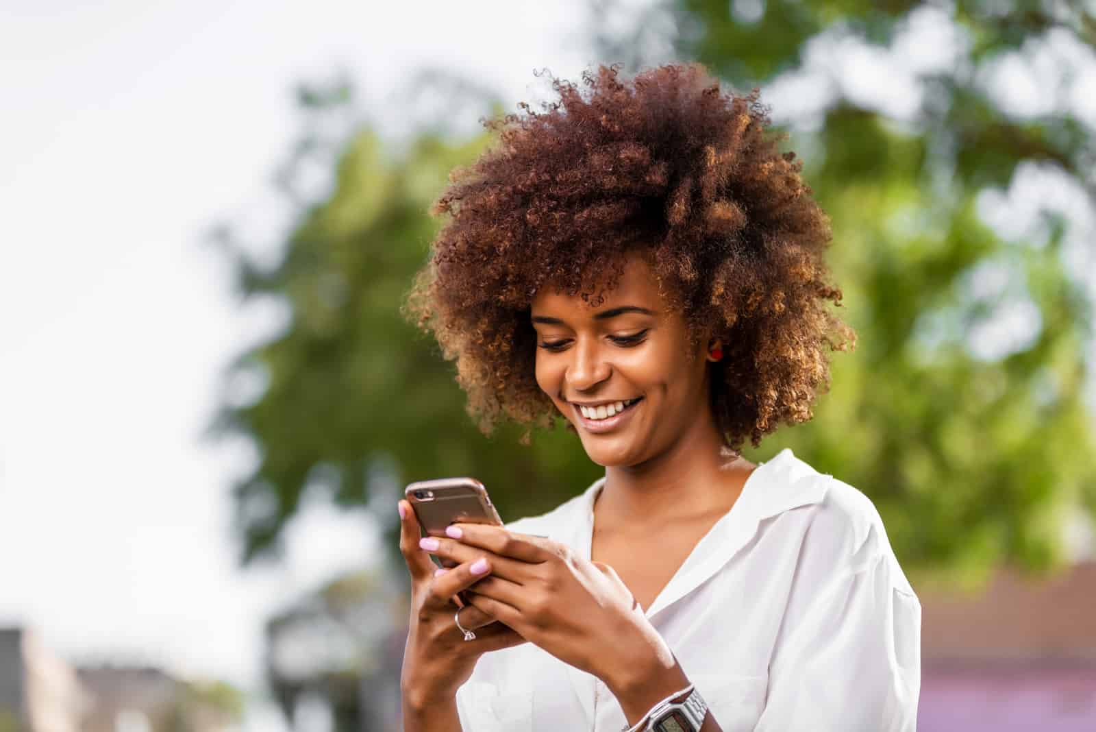 smiling woman with curly hair texting outdoor