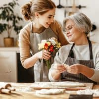 Grandaughter giving flowers to her grandma and smiling indoors