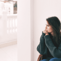 pensive woman sits on the couch and looks out the window