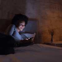 a smiling woman is lying on the bed and typing on the phone