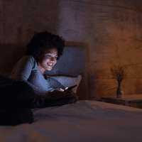 una mujer sonriente está tumbada en la cama y tecleando en el teléfono