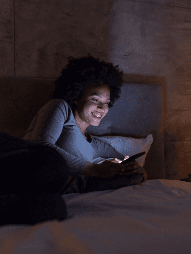 a smiling woman is lying on the bed and typing on the phone