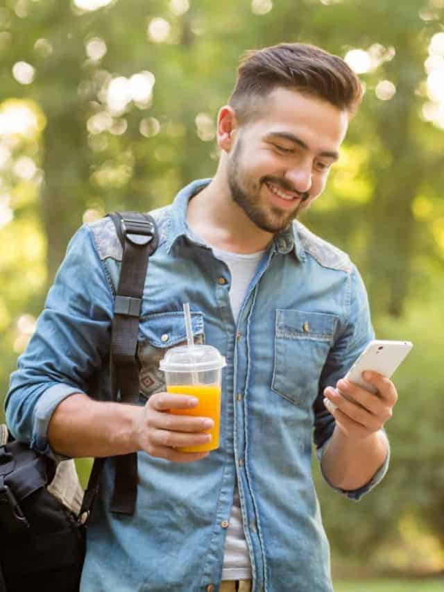 smiling man holding juice in one hand and mobile phone in other hand