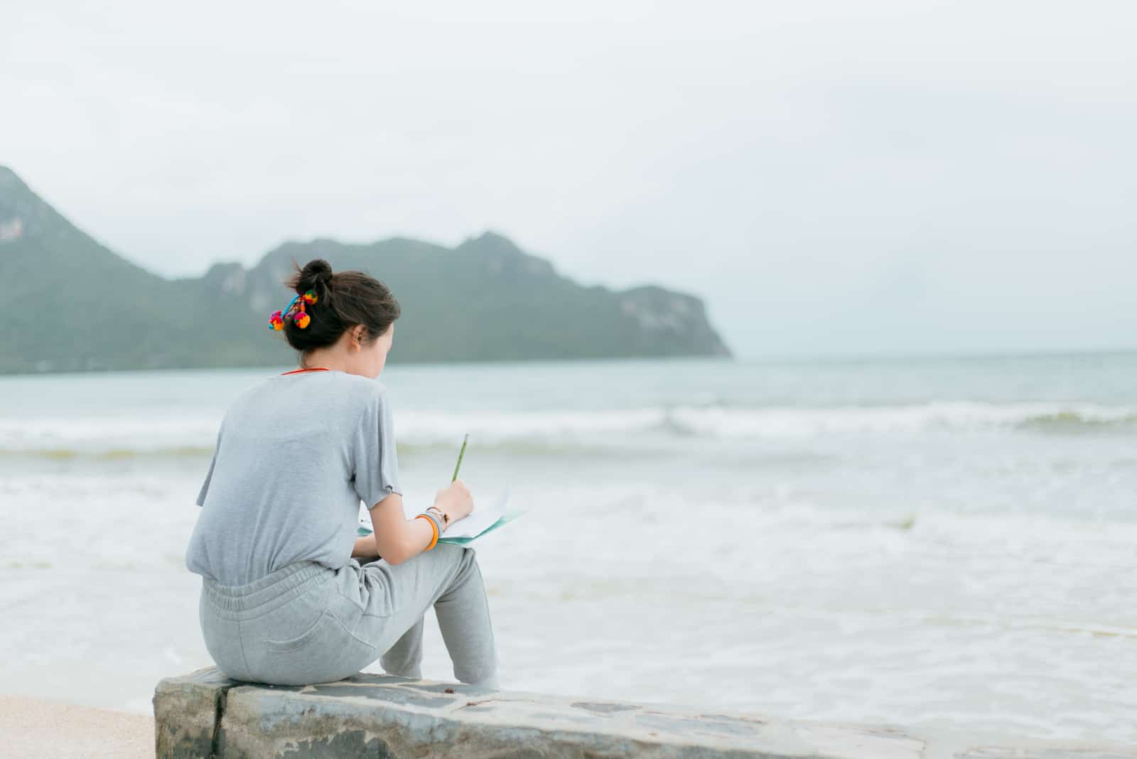 mujer sentada en la playa y escribiendo en un cuaderno