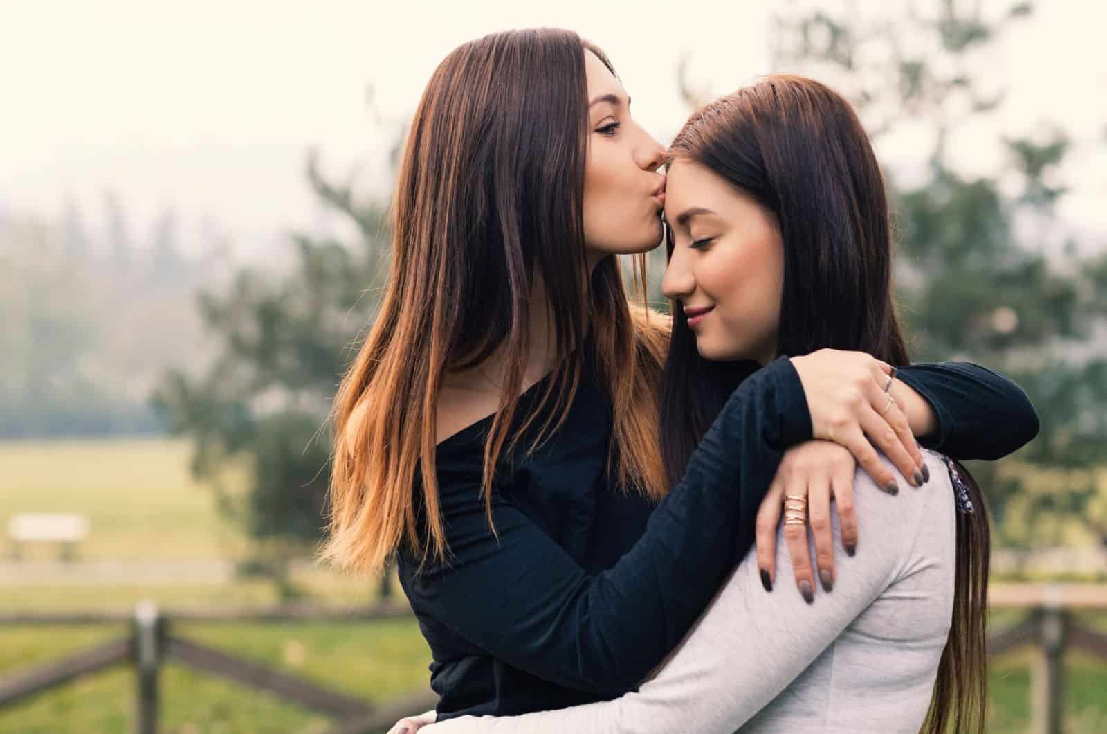 young sisters hugging and kissing outdoors in a park
