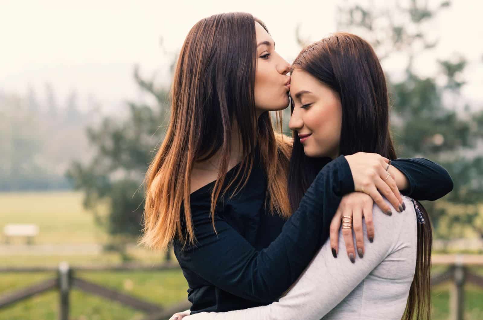 hermanas jóvenes abrazándose y besándose al aire libre en un parque