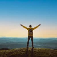 Hiker with arms up standing on the top of the mountain