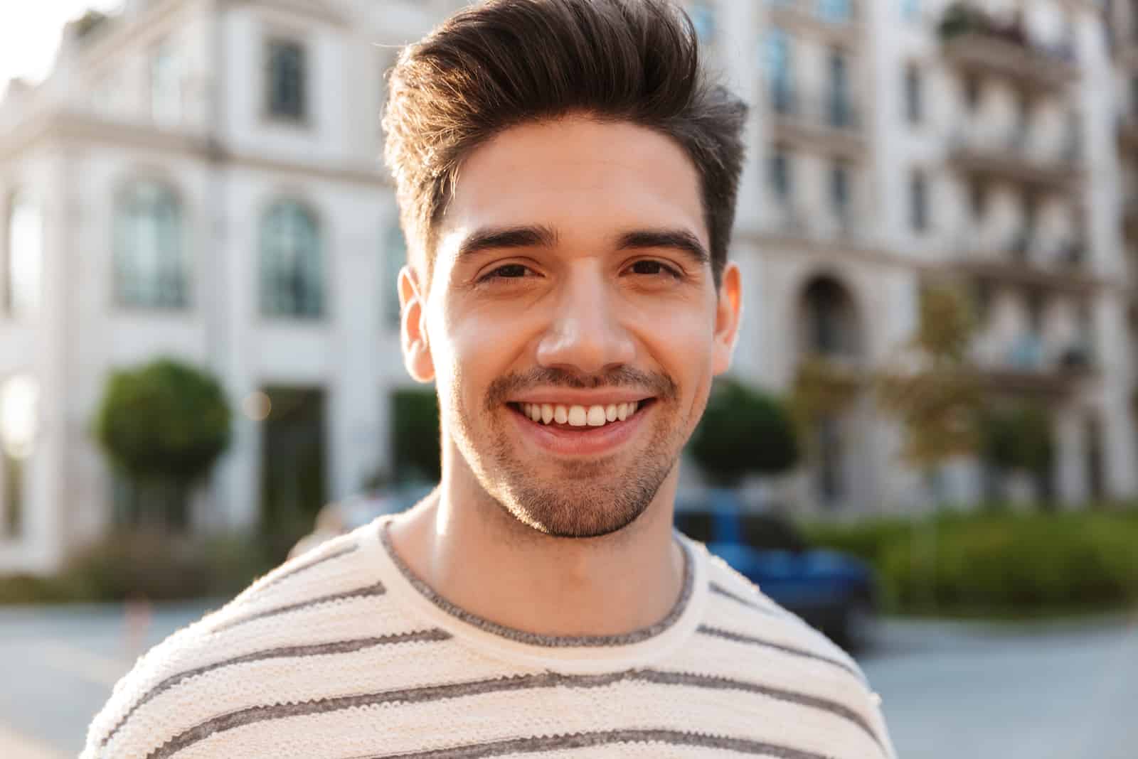 handsome man smiling and looking at camera while walking at city street