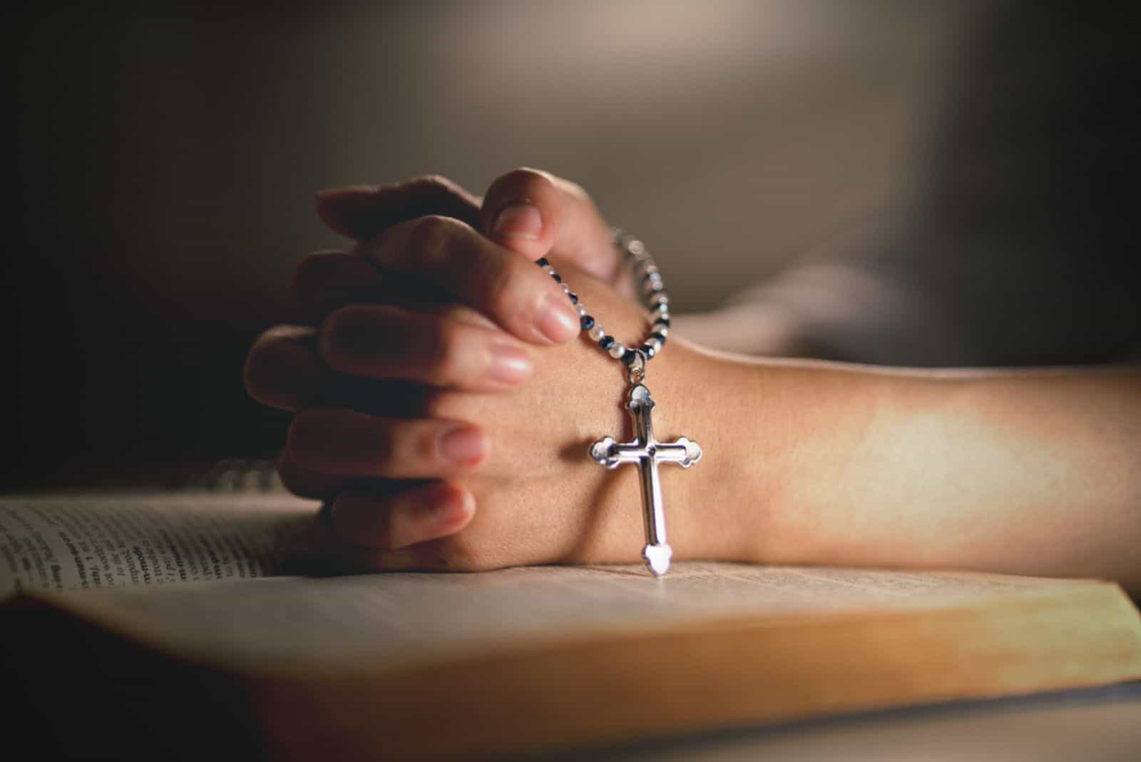 hands of religious christian woman holding jusus cross rosary praying to god with holy bibble