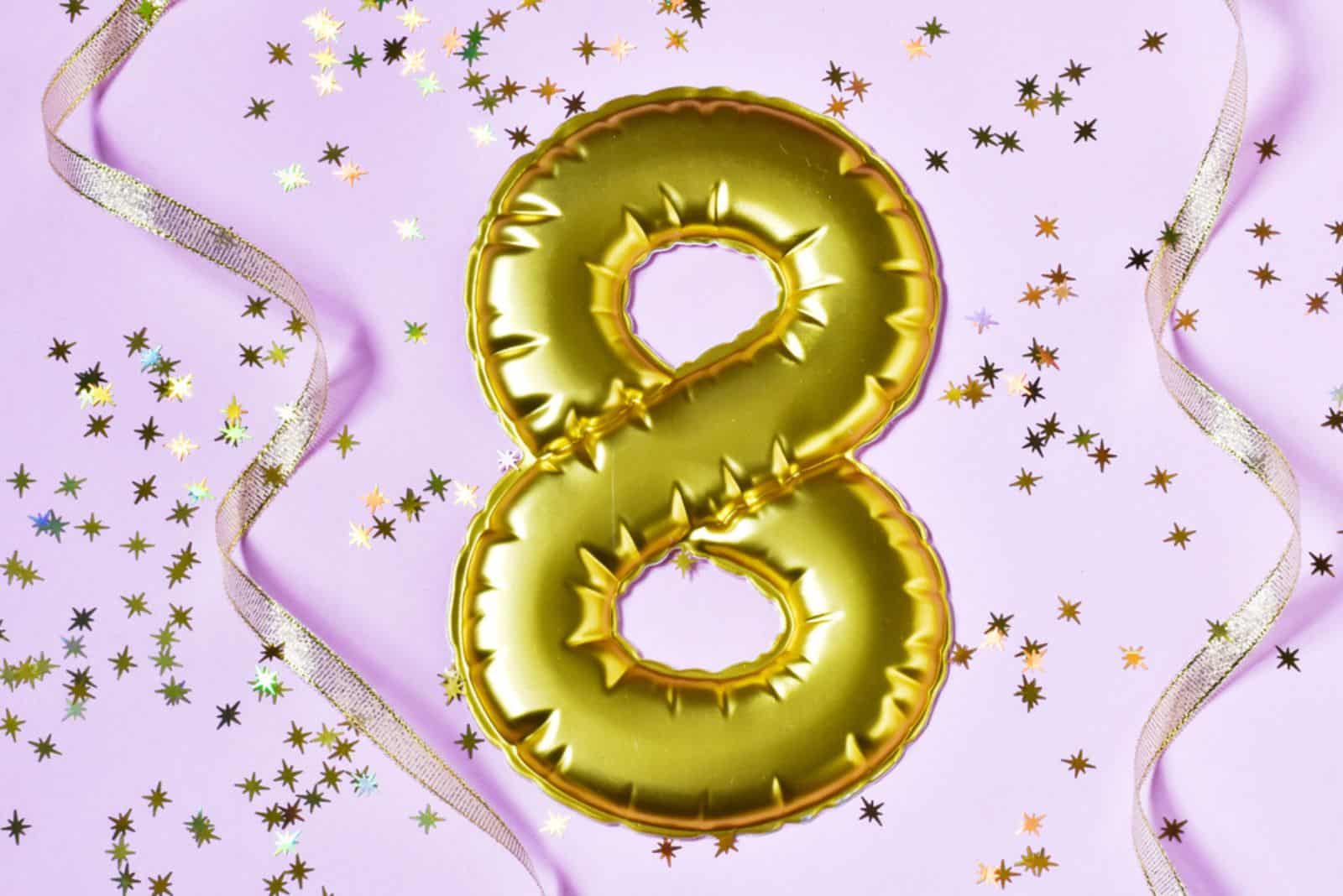 Numeral 8 with gold ribbon and confetti on a pink background