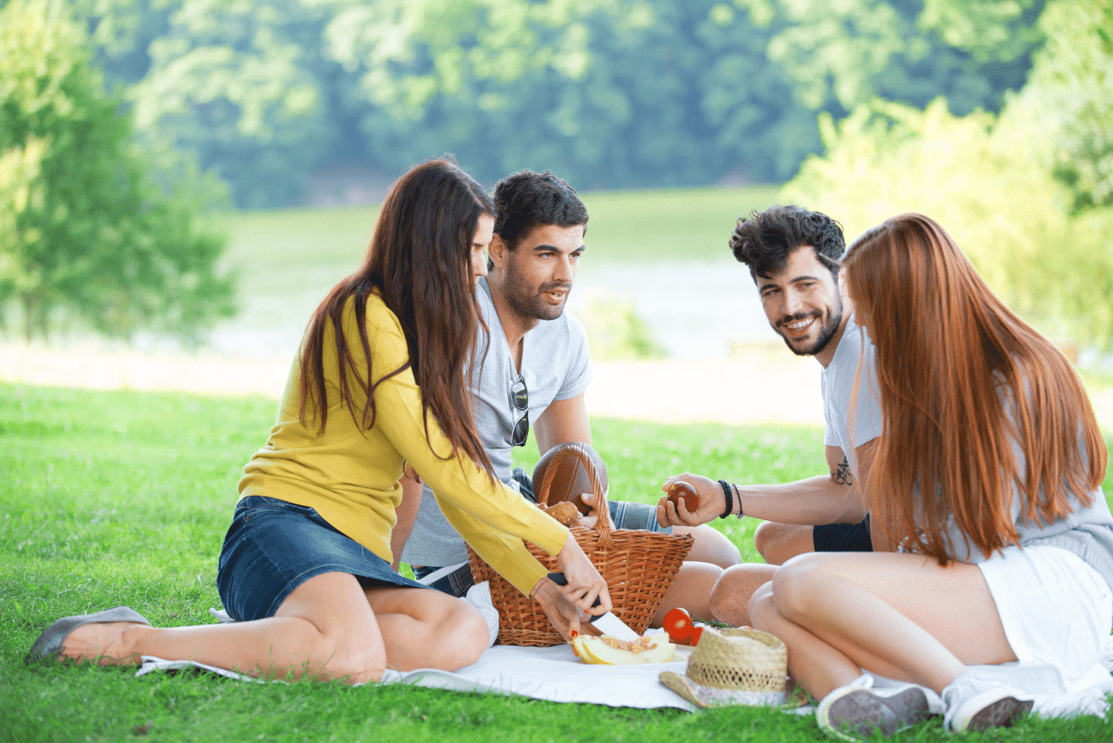 smiling friends are sitting and eating in the meadow