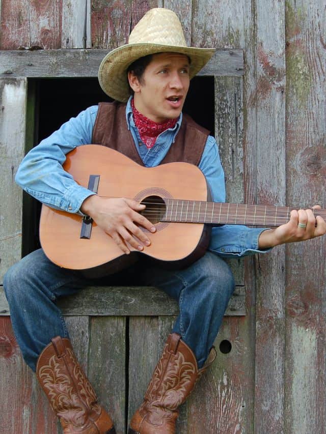 a man with a cowboy hat and boots sitting and holding a guitar