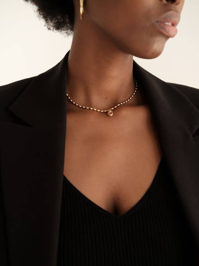 a woman with a golden earrings and necklace in black blazer