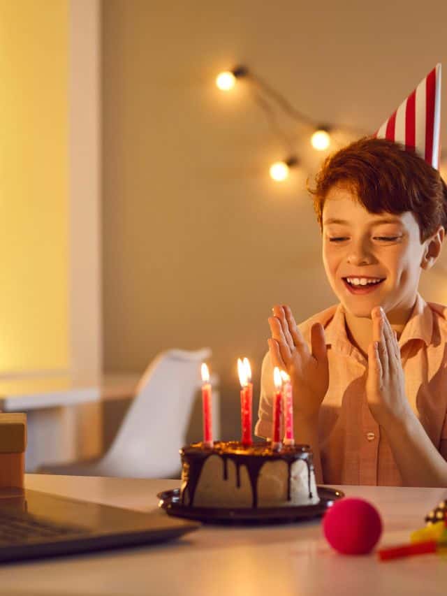 boy in a beige shirt with birthday hat and birthday cake smiling